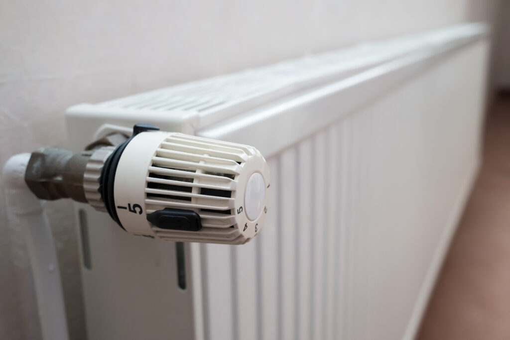 Radiator with thermostat and the ability to turn the knob and reduce the heating temperature. Concept of crisis and increase in heating costs. Close-up.
